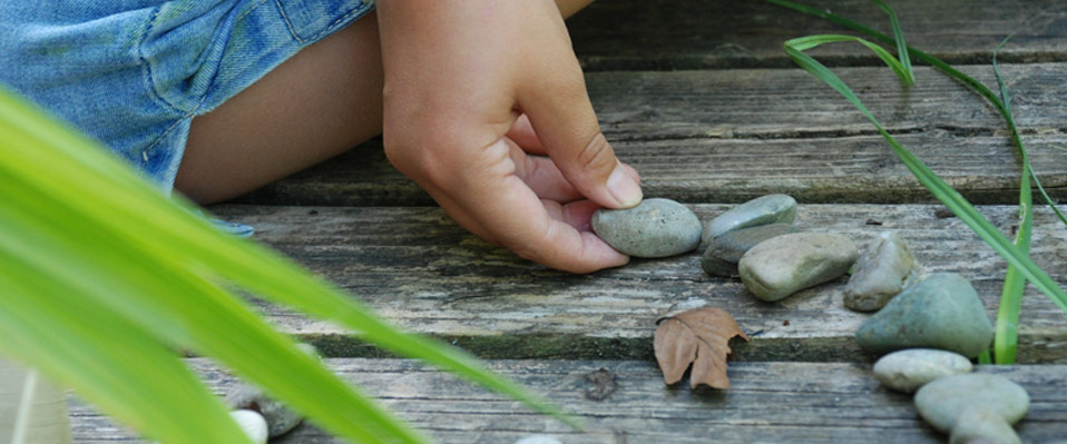 Eine Hand legt besonnen Steine in Form eines Herzens auf Holzdielen am Boden